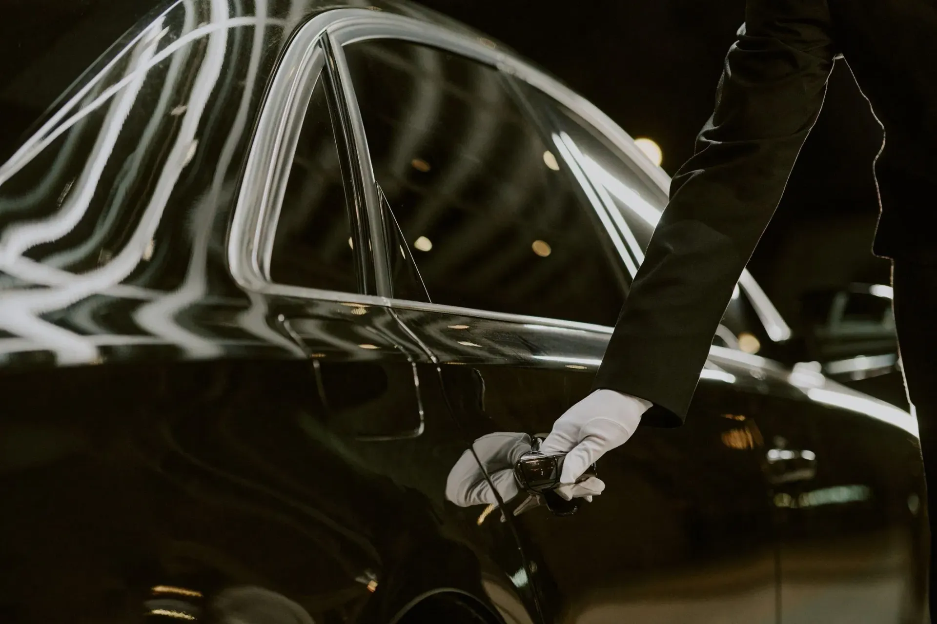A chauffeur opens the door of a polished black executive sedan